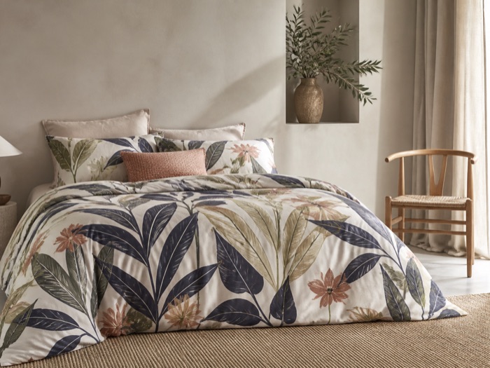 Printed botanical bedding in a lime-plaster bedroom with olive branches and linen curtains.