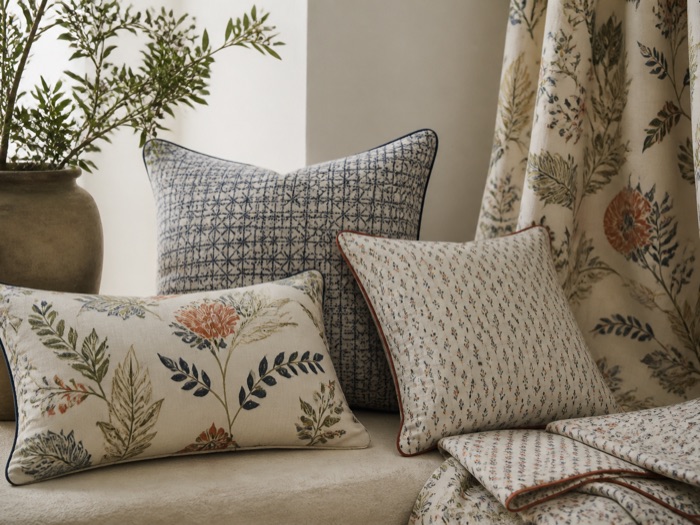 Printed cushions and a botanical curtain fabric arranged against a plaster wall.