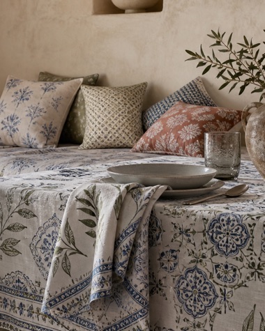 Stacked printed cushions in indigo, olive and terracotta against a lime-plaster wall.