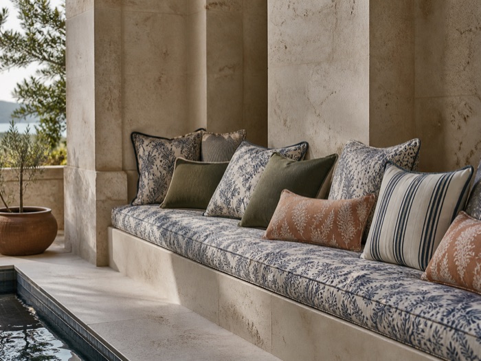 Printed outdoor cushions on a stone bench beside a pool, with an olive tree beyond.
